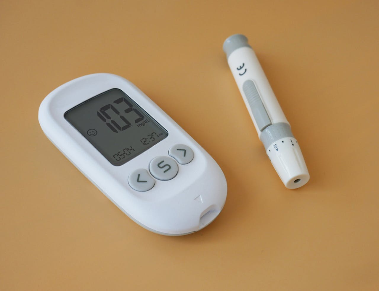 Close-up of a digital blood glucose meter and lancet pen on a brown surface.