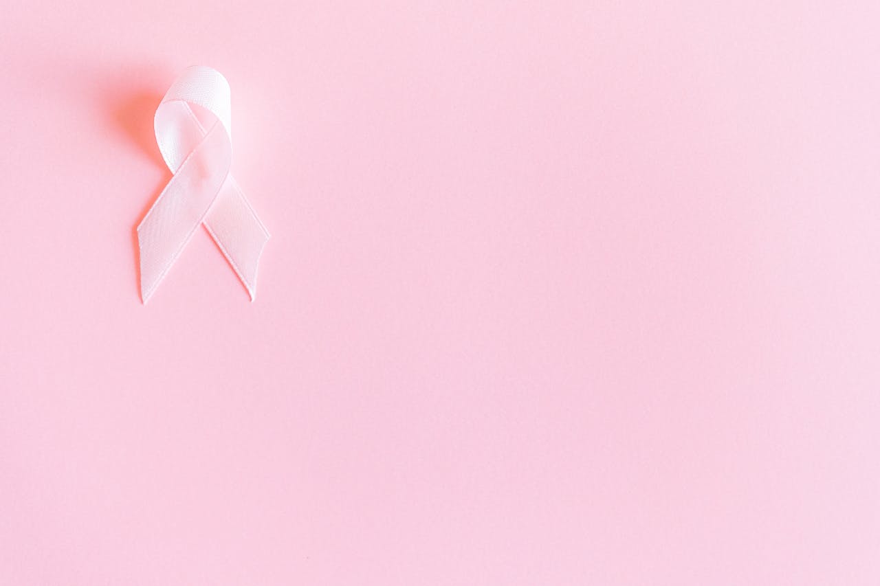 A pink ribbon on a soft pink background symbolizing breast cancer awareness and solidarity.